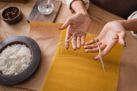 Photo for Partial view of african american woman holding twine near wax sheet and wooden plate with grated beeswax in workshop - Royalty Free Image