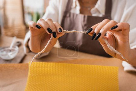 vista parcial de mujer afroamericana borrosa sosteniendo cordel natural cerca de hoja de cera y papel artesanal en taller