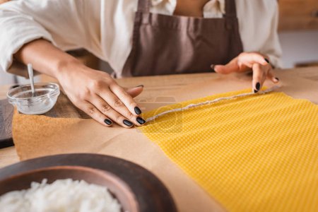 partial view of african american woman in apron holding natural twine near wax sheet on parchment in craft workshop