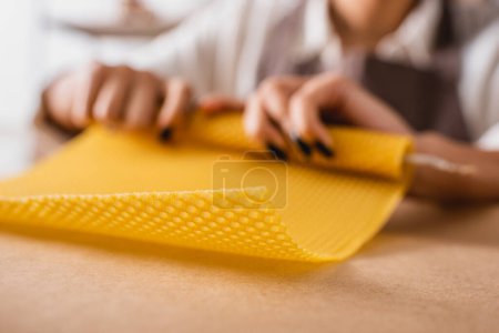 partial view of african american craftswoman rolling natural wax sheet on blurred background