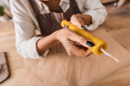 high angle view of cropped african american craftswoman holding homemade candle on blurred background