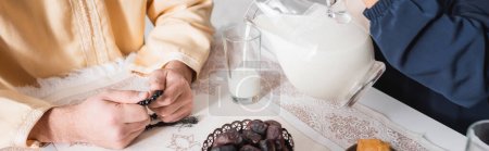 Photo for Cropped view of muslim woman pouring milk near husband during suhur in morning, banner - Royalty Free Image