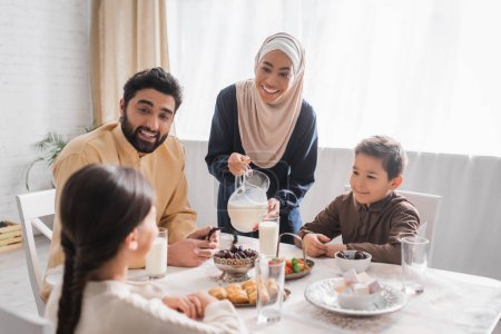 Foto de Sonriente familia musulmana mirando a su hija durante el desayuno suhur en casa - Imagen libre de derechos