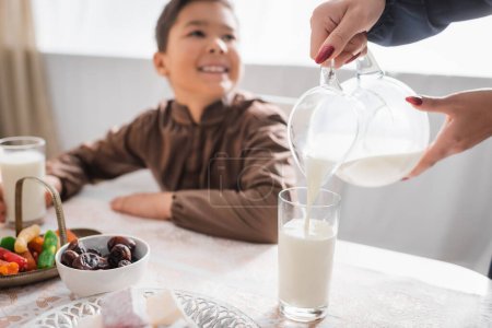 Photo for Muslim mother pouring milk during suhur breakfast near blurred son at home - Royalty Free Image