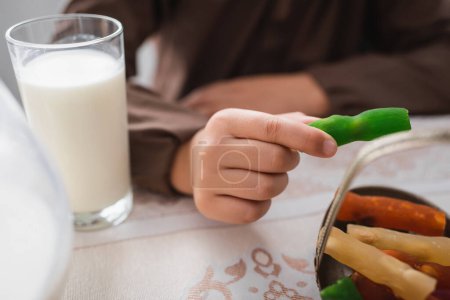 Foto de Cropped view of muslim boy holding cevizli sucuk near glass of milk during suhur breakfast - Imagen libre de derechos