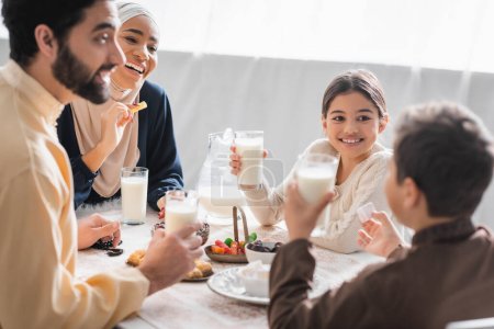 Foto de Positive muslim family holding glasses of milk and talking near food during suhur at home - Imagen libre de derechos