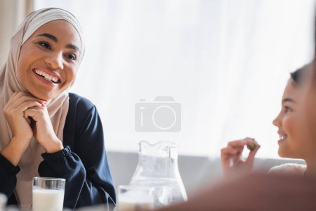 Photo for Happy african american mother in hijab looking at blurred kids during suhur at home - Royalty Free Image