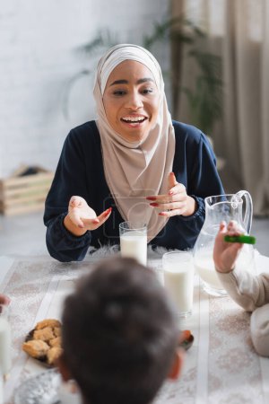 Photo for Smiling african american mother in hijab talking to kids during suhur breakfast at home - Royalty Free Image