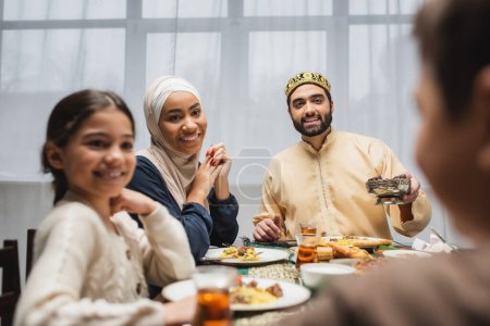 Photo for Positive middle eastern family looking at blurred boy during ramadan dinner - Royalty Free Image