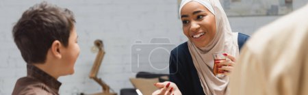Téléchargez les photos : Mère afro-américaine en hijab tenant du thé et parlant à son fils à la maison, bannière - en image libre de droit