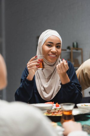 Téléchargez les photos : Femme afro-américaine dans le hijab tenant le thé pendant le dîner ramadan à la maison - en image libre de droit
