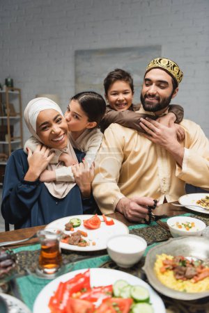 Photo for Cheerful middle eastern family hugging near food during ramadan at home - Royalty Free Image