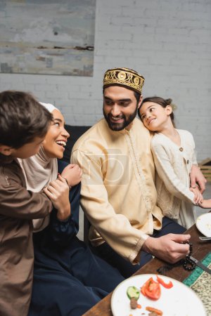 Téléchargez les photos : Homme arabe souriant étreignant sa fille et regardant sa famille pendant le ramadan à la maison - en image libre de droit
