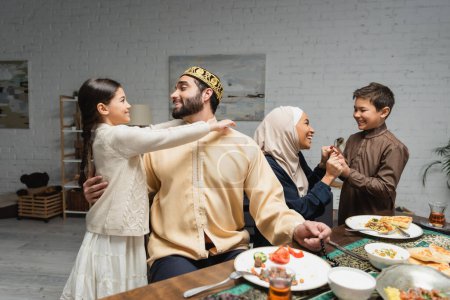 Photo for Cheerful middle eastern family hugging and talking during ramadan dinner at home - Royalty Free Image