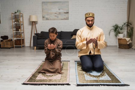 Foto de Padre e hijo musulmanes rezando sobre alfombras en casa - Imagen libre de derechos