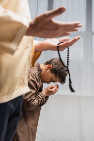 Photo pour Garçon du Moyen-Orient priant près du père avec des perles de prière pendant le ramadan à la maison - image libre de droit