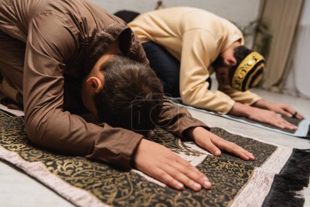 Téléchargez les photos : Enfant musulman priant sur le tapis près du père pendant la salah à la maison - en image libre de droit