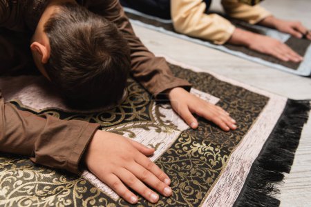 Foto de Niño árabe rezando en la alfombra durante la salah ramadán en casa - Imagen libre de derechos