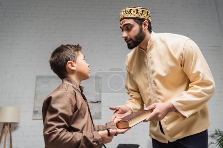 Photo for Middle eastern father giving book to preteen son with prayer beads at home - Royalty Free Image