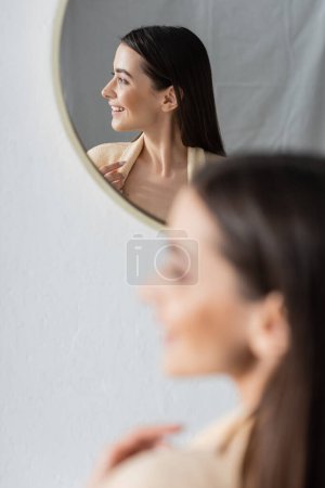 Foto de Reflection of smiling young woman looking away in bathroom mirror - Imagen libre de derechos