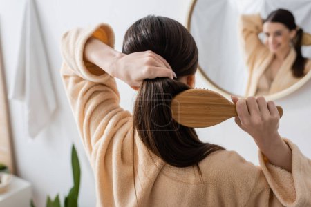 Foto de Back view of young brunette woman brushing hair in bathroom - Imagen libre de derechos