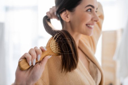 Photo for Smiling and blurred young woman brushing shiny hair in bathroom - Royalty Free Image