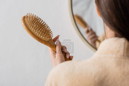 abgeschnittene Ansicht einer jungen Frau mit Haarbürste in der Nähe eines verschwommenen Spiegels im Badezimmer 