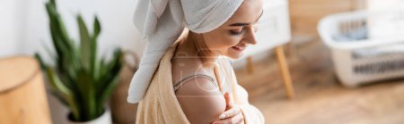Photo for Happy young woman in bathrobe with towel on head applying body butter, banner - Royalty Free Image