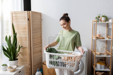 Lächelnde junge Frau hält Korb mit Wäsche zu Hause 