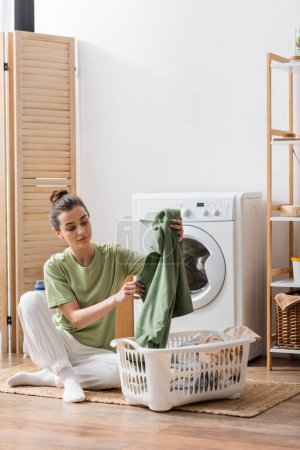 Foto de Young woman taking clothes from basket in laundry room - Imagen libre de derechos