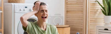 sad woman touching head and crying in laundry room, banner 