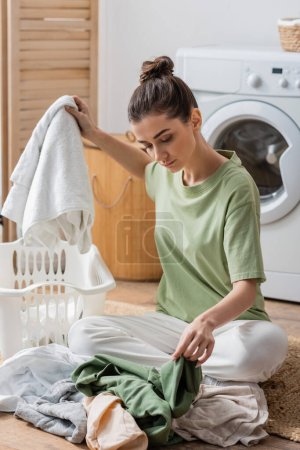 Young woman sorting clothes on floor in laundry room 