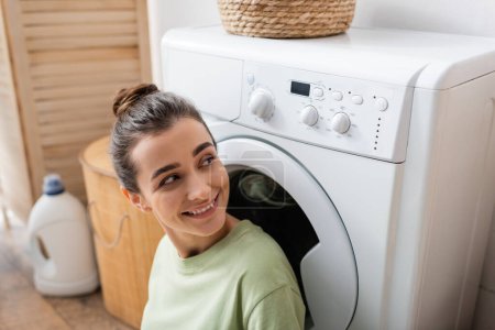 Smiling woman looking at washing machine at home