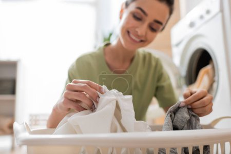 Blurred woman taking clothes from basket in laundry room 