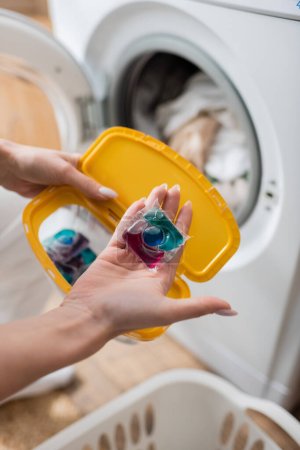 Ausgeschnittene Ansicht einer Frau, die Waschmittel und Schachtel in der Nähe einer Maschine in der Waschküche hält 