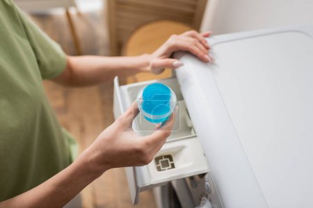 Cropped view of woman holding cap with liquid cleaner near washing machine 