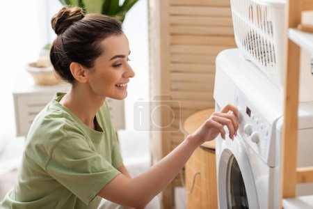 Mujer joven positiva cambiando la lavadora en casa 