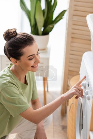 Young brunette woman switching washing machine in laundry room 