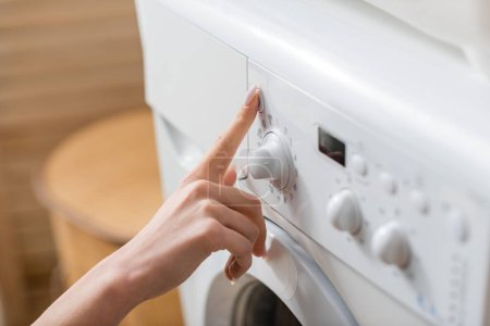 Vista recortada de la mujer pulsando el botón de la lavadora en la sala de lavandería  