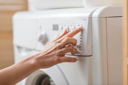 Cropped view of woman tuning white washing machine in laundry room 