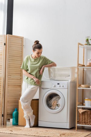 Jeune femme regardant la blanchisserie dans la machine à laver dans la buanderie 