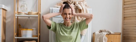 Angespannte Frau berührt Kopf neben Waschmaschine in Waschküche, Banner 