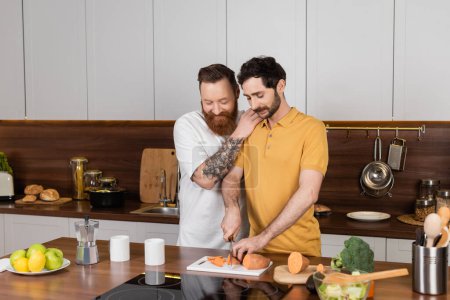 sonriente gay hombre abrazando pareja cocinar en cocina en casa 
