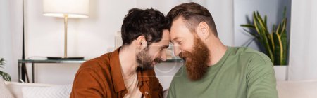 Photo for Side view of bearded gay couple sitting on couch at home, banner - Royalty Free Image