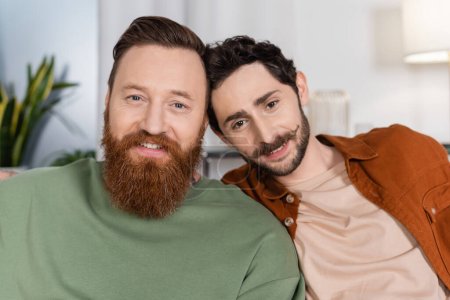Foto de Retrato de sonriente pareja del mismo sexo mirando a la cámara en casa - Imagen libre de derechos