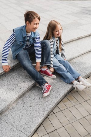 in voller Länge fröhliche, gut gekleidete Kinder, die auf den Treppen der städtischen Straße sitzen 