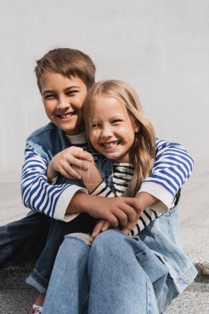happy preteen boy in hugging well dressed girl while sitting on stairs 