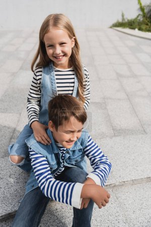 pleased girl in stylish clothes leaning on shoulders of well dressed boy 