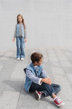 full length of well dressed girl in denim outfit standing near boy on blurred foreground 