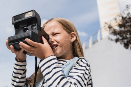 Niederwinkelaufnahme eines Mädchens in Jeansweste und gestreiftem Langarmshirt, das ein Foto der Vintage-Kamera macht 
